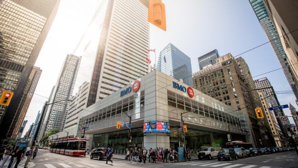 A busy intersection on Bay Street in downtown Toronto, showing a BMO bank building, streetcar and tall office towers