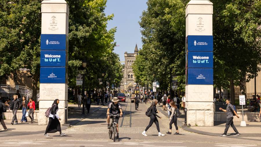 Entrance to U of T front campus with people talking in front of the U of T entrance gates and someone riding a bicycle