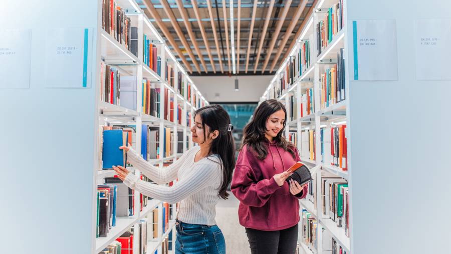 Two students in the stacks of a modern library looking through books
