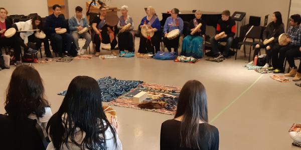 A large group of students and community members sitting in an Indigenous drumming circle
