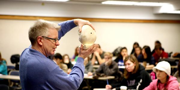 A professor holding an object and showing it at the front of a classroom