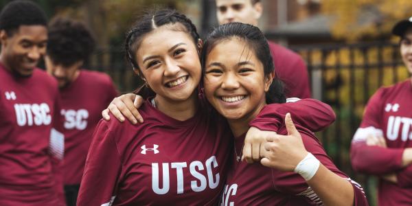 Two student athletes with their arms around each other. One of them is giving a thumbs up.
