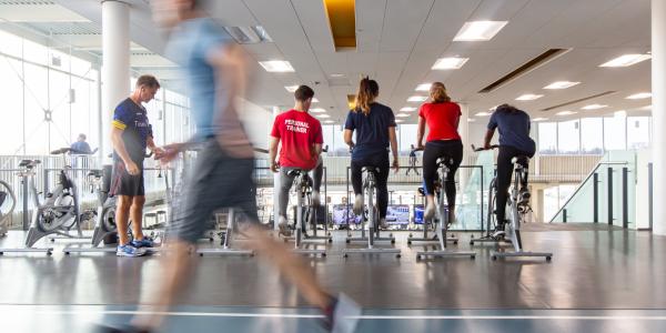 Student running on a track, and students using spin bikes.
