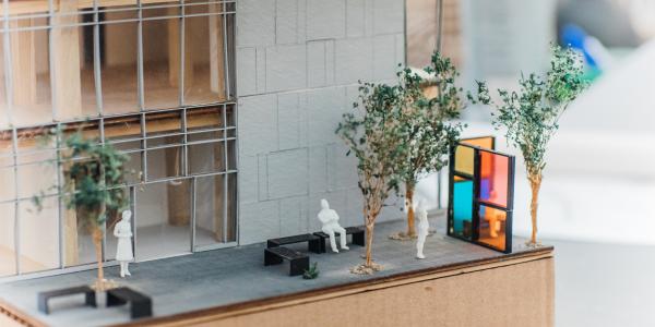 A close-up of a detailed architectural model of a modern building, featuring miniature trees, benches, and small human figures