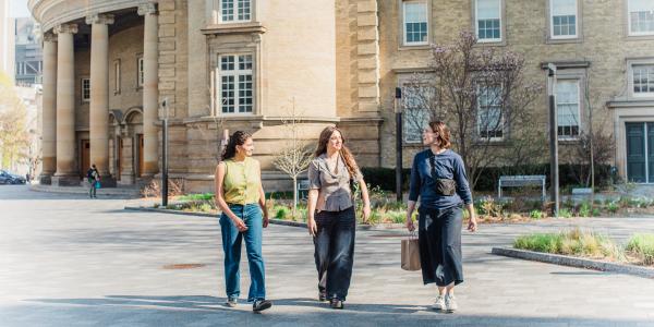 Three students walking together on a sunny day in front of Convocation Hall at the University of Toronto