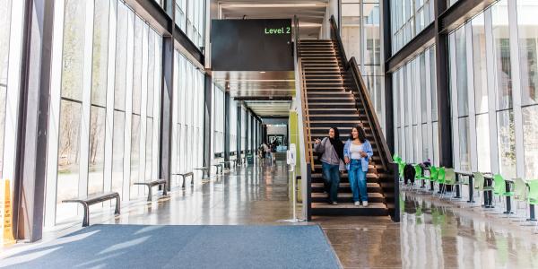 Two students walk down a staircase in a bright, glass-walled building