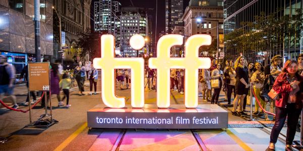 A neon TIFF (Toronto International Film Festival) sign in the middle of the street with people walking around it