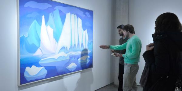 A group of people view a large, vibrant painting of icebergs in a gallery