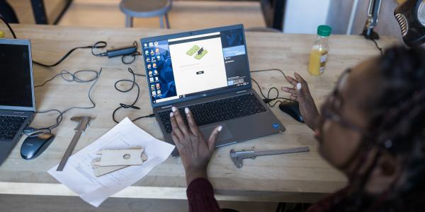 Student working on a 3D model design on a laptop in a lab workspace