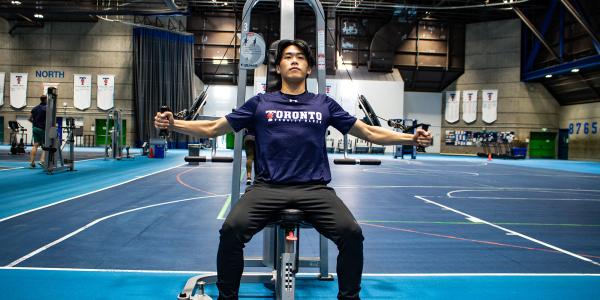 Student using exercise machine in gym.