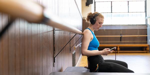 Student kneeling on floor of dance studio, looking at her phone.
