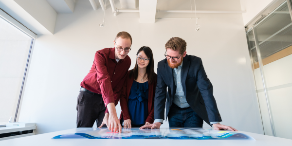 Three people in suits looking at a plan on a table.