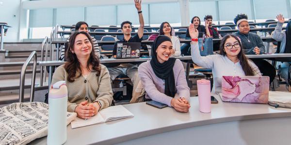 Students in lecture hall raising hands.