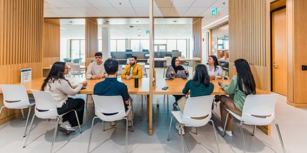 A group of students sitting around two connected wooden tables engaged in conversation