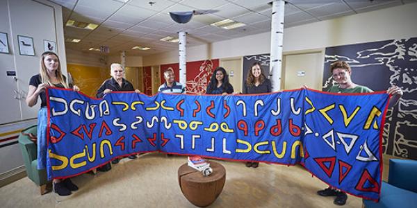 Students and faculty holding up a long blue banner with Indigenous writing on it