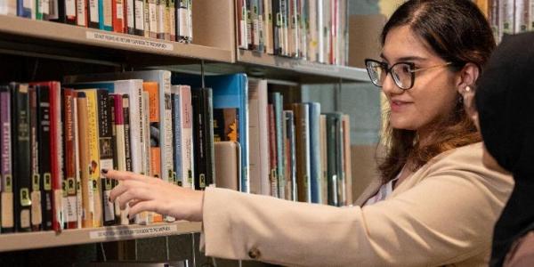 Two students pointing at books on shelf.
