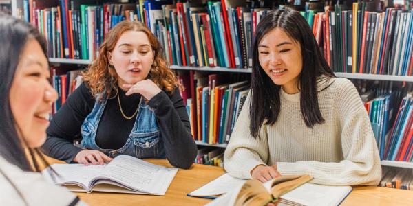 Three students reading books in a library.