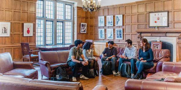 Five students sitting on couches indoors, laughing and talking to one another