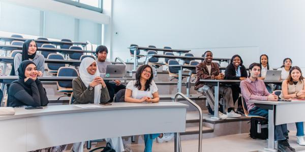 A small class of students sitting in a lecture hall, smiling.