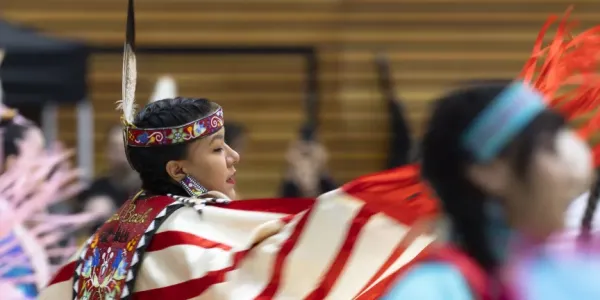 Indigenous dancer performs at a powwow, wearing vibrant colours, beadwork and feathers