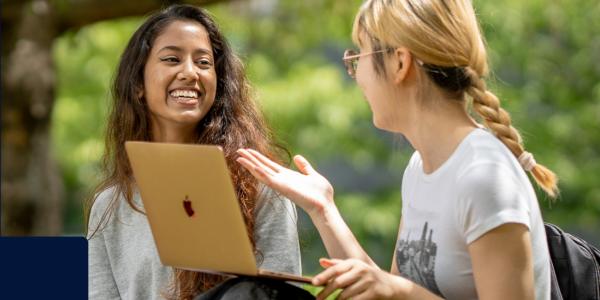 Two students chatting outside in front of a laptop.