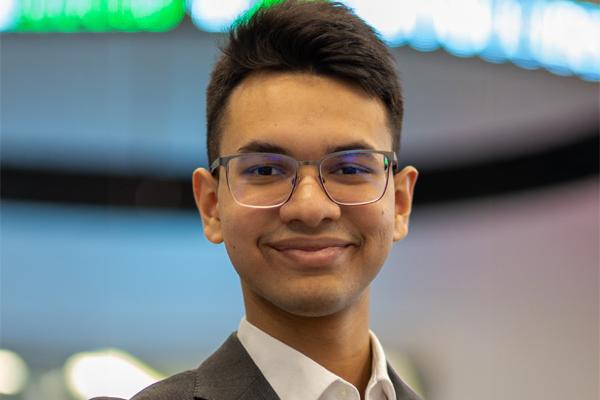 Student smiling at the camera wearing glasses and a suit with no tie