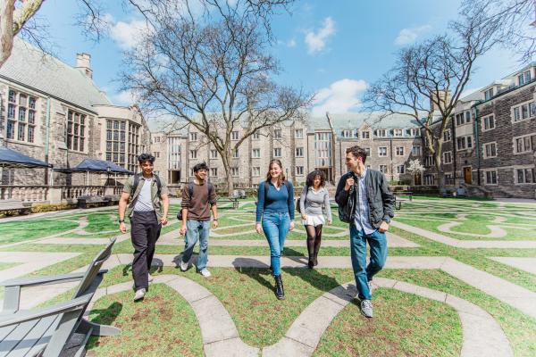Five students walking through a Trinity Quad, surrounded by a historic stone building