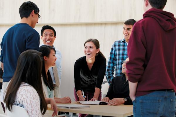 Students gather around a table, smiling and collaborating