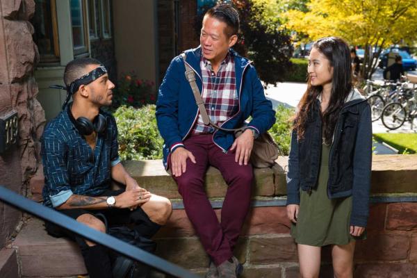 Three students sitting on the steps of a brown brick building having a discussion