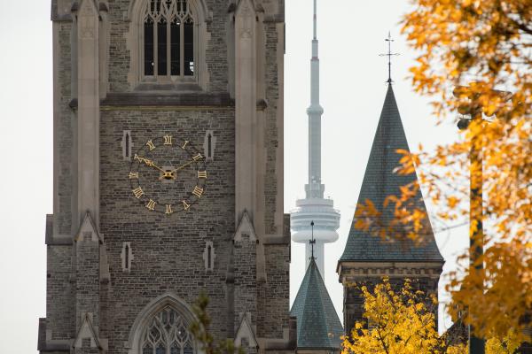 The clock on a tower with the CN Tower behind it