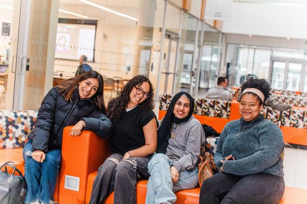 Four smiling students sit together on bright orange couches 