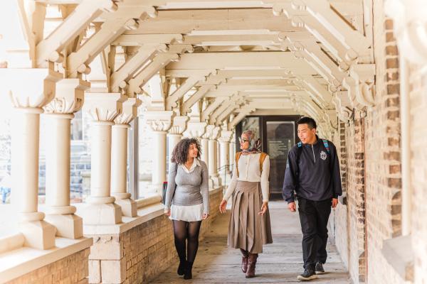 Three students walking and talking together in a covered outdoor walkway with columns