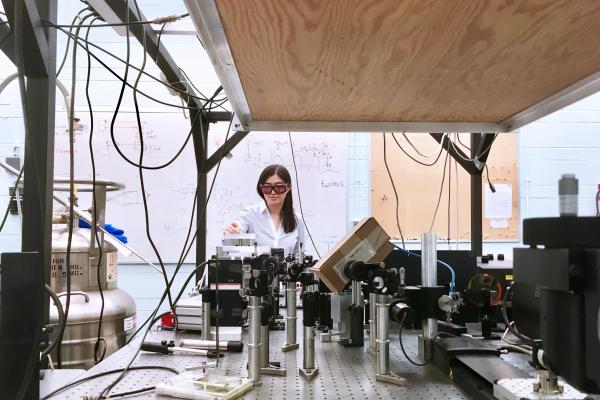 Professor wearing safety glasses working with equipment in a physics lab, surrounded by wires