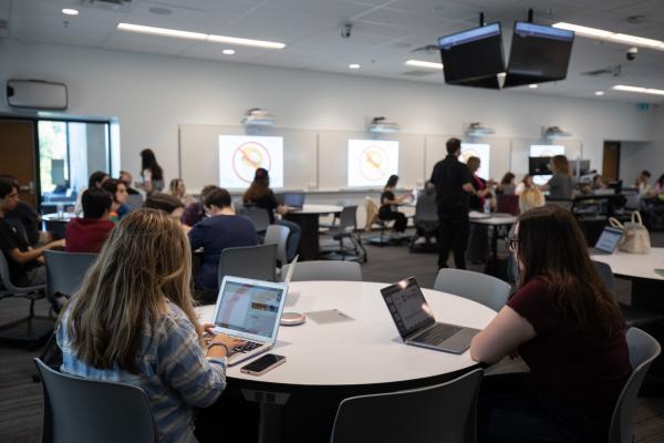 Students working on laptops in a classroom during a presentation