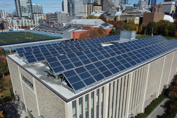 A rooftop covered with solar panels, with a sports field and downtown Toronto skyline visible in the background
