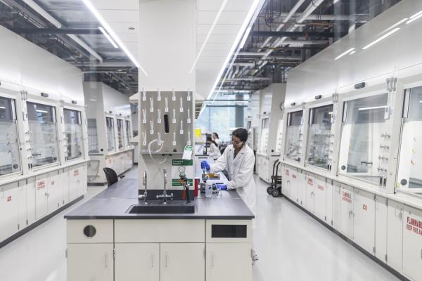 Scientist in a white lab coat working in a modern laboratory with fume hoods lining both walls