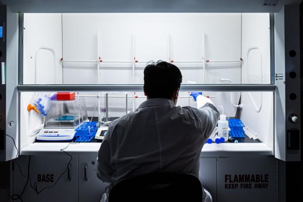 Person in a lab coat working at a laboratory fume hood with scientific equipment