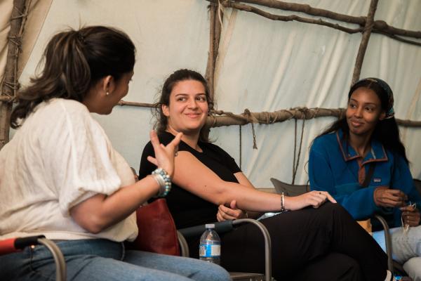 Three students sitting and talking inside a structure made of wood and canvas
