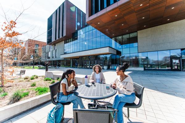Three students sitting together outside at a patio table, talking and laughing with each other