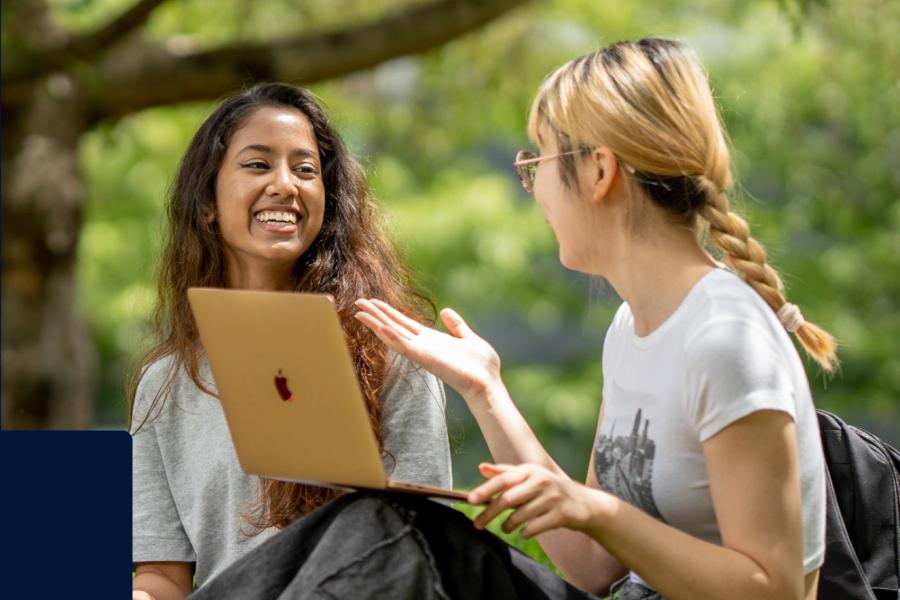 Two students chatting outside in front of a laptop.