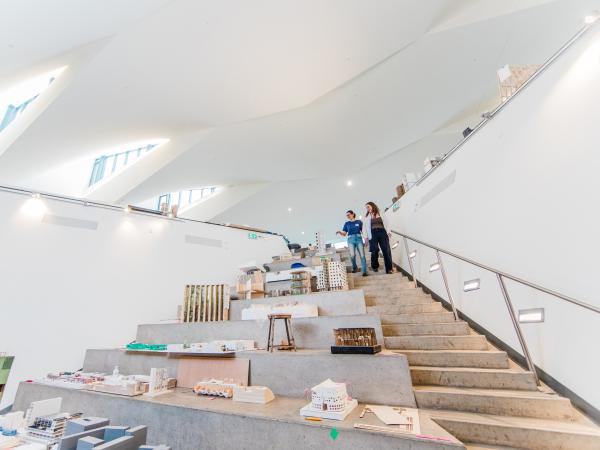 Students view architectural models displayed on tiered steps inside a modern building