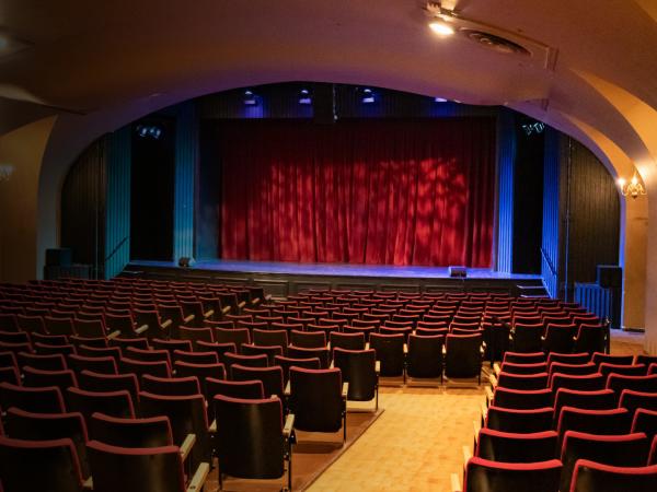 An empty theatre with a lit stage and red curtain