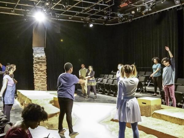 Students rehearse on stage in a black box theatre, surrounded by rows of seating