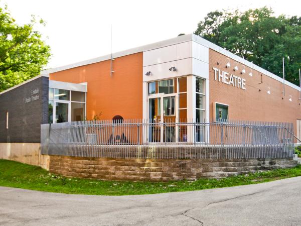 Exterior view of a modern, low-rise theatre building surrounded by greenery with the The word "THEATRE" on the upper wall