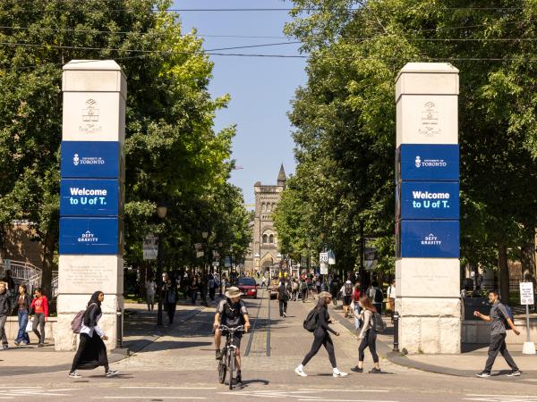 Entrance to U of T front campus with people talking in front of the U of T entrance gates and someone riding a bicycle