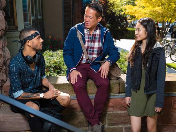 Three students sitting on the steps of a brown brick building having a discussion