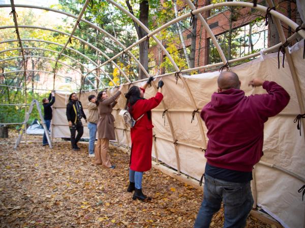 A group a students putting the outside layer on the frame of a teaching lodge