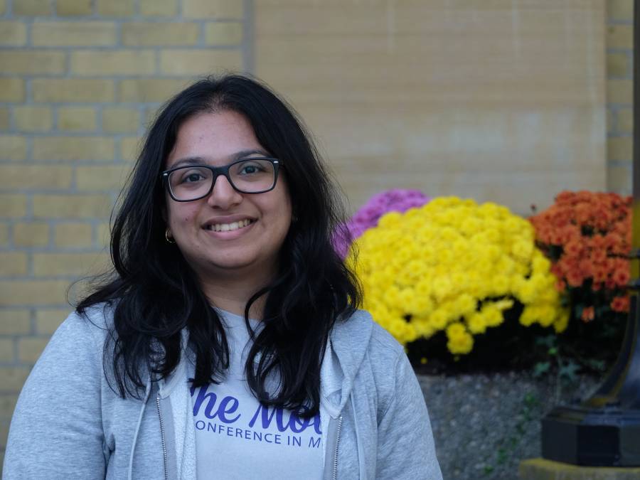 Smiling student standing outside in front of some flowers
