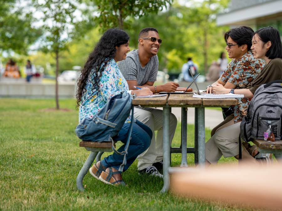 Four students sitting at a picnic bench chatting with each other