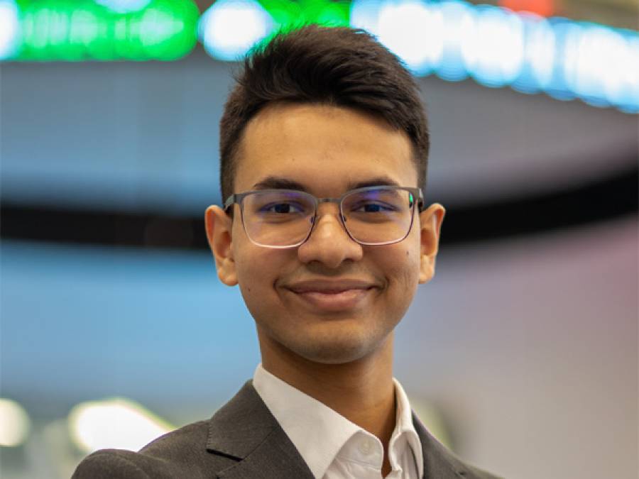 Student smiling at the camera wearing glasses and a suit with no tie